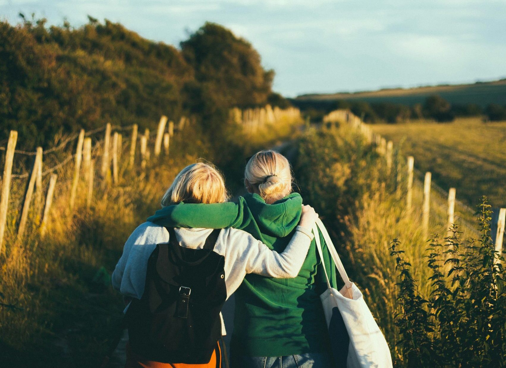 Two friends walking down a hiking path lined with trees with their arms around each other.